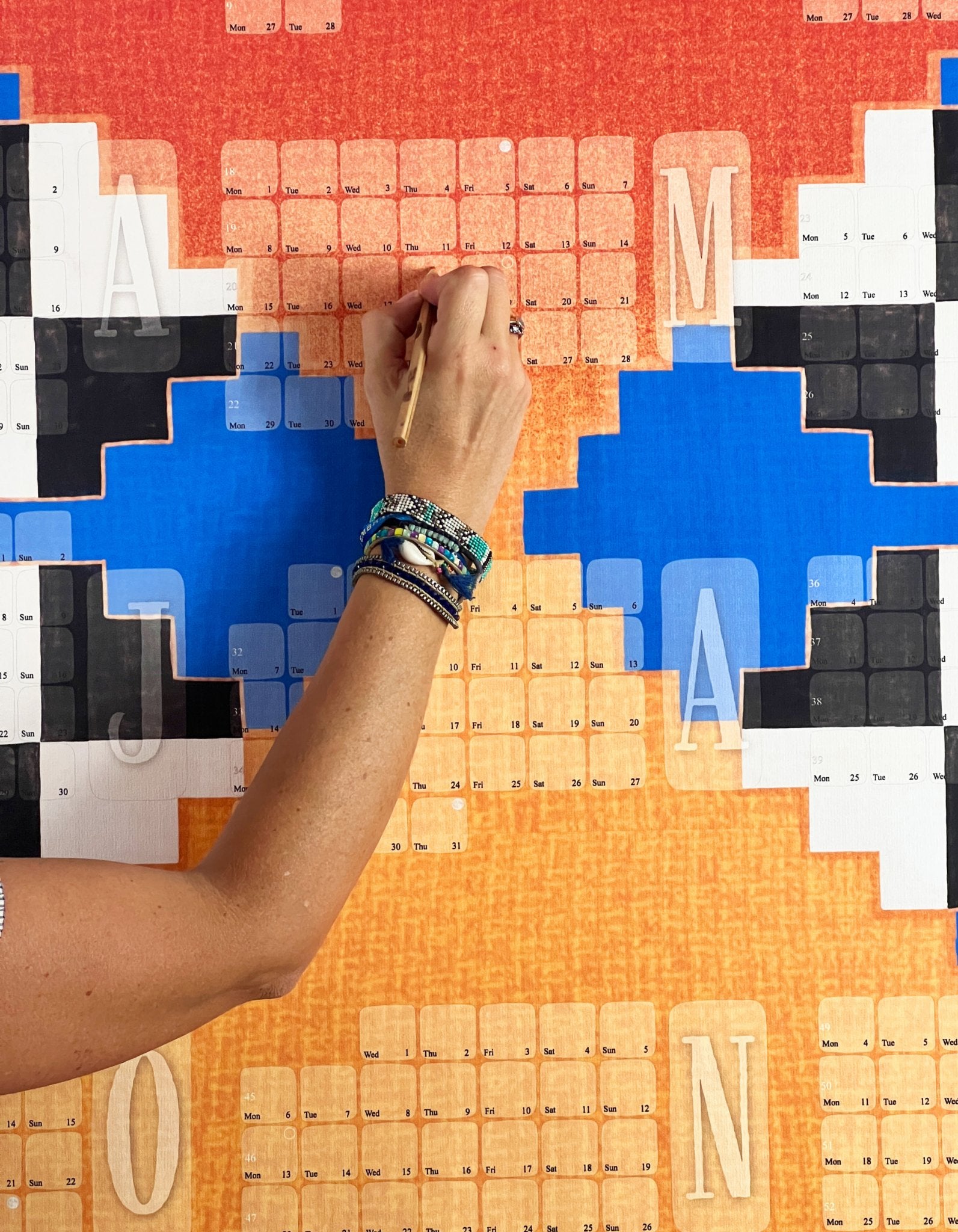 Nahaufnahme des Wandkalenders Mexico orange mit einer Hand, die gerade hineinschreibt 